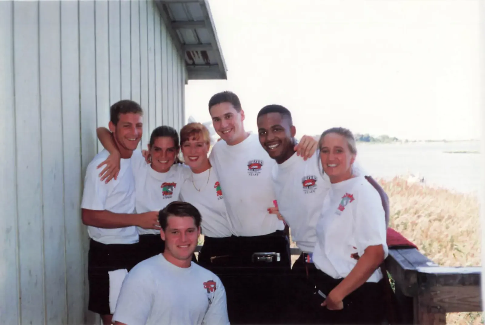 A group of Hooper's Crab House crew members in matching shirts gathered outside by the bay