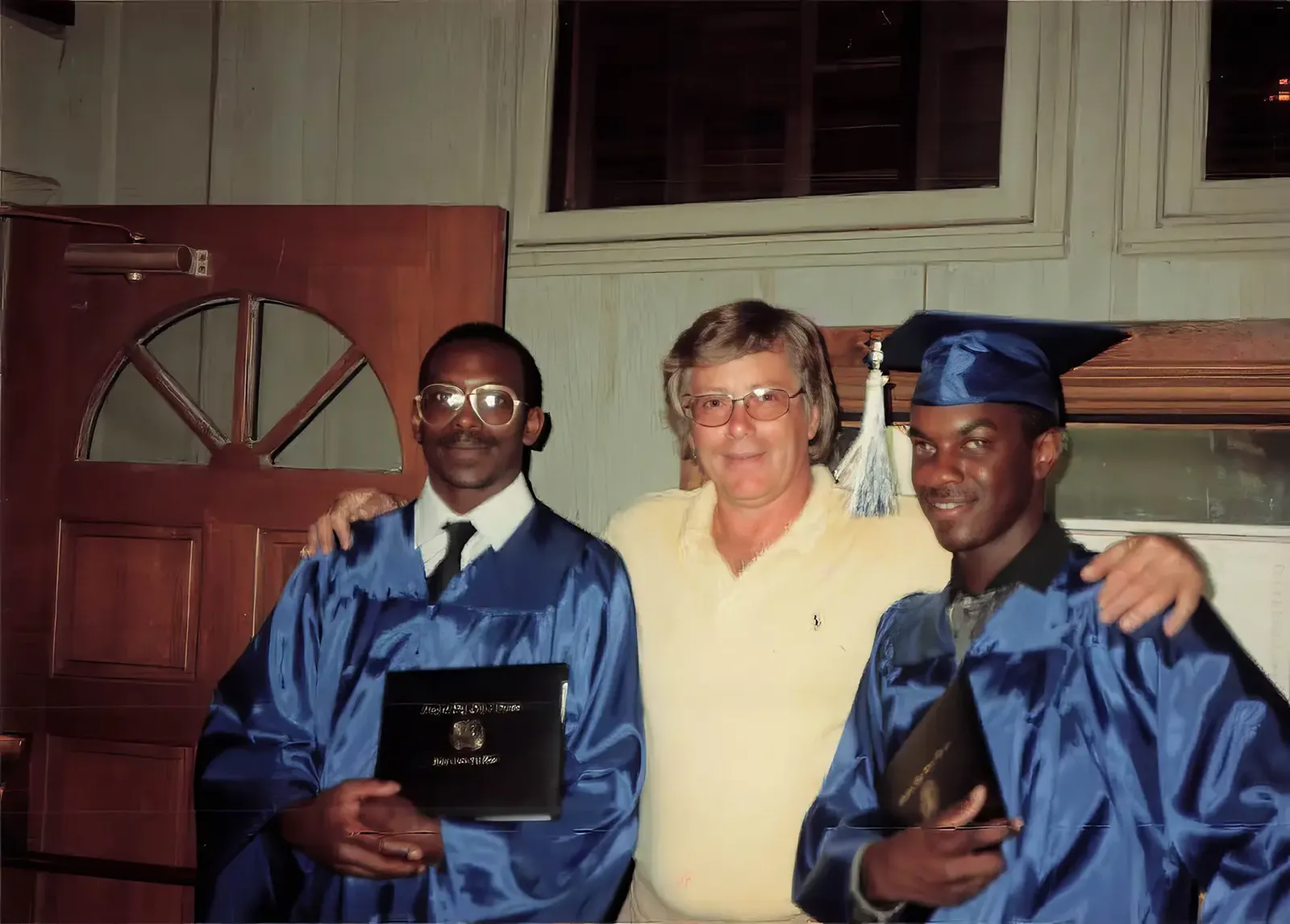 Pete Shepherd standing between two Hooper's team members in blue graduation caps and gowns, holding their diplomas