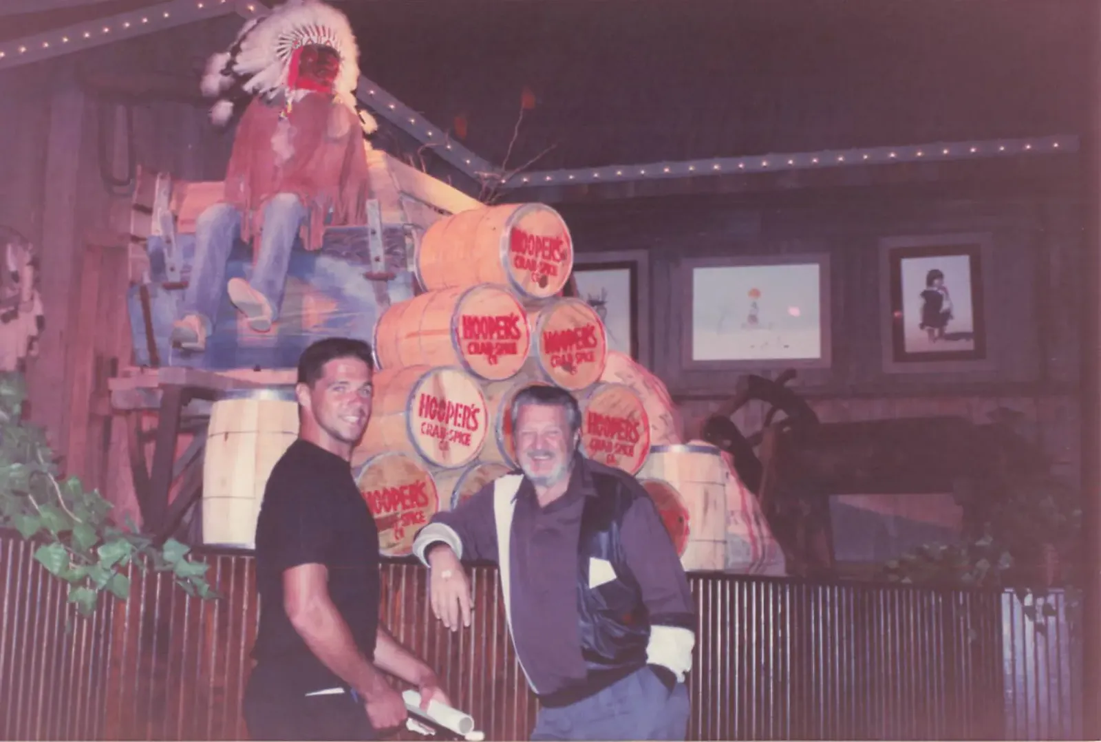 Pete Shepherd standing with a staff member in front of stacked Hooper's Crab Spice barrels at the restaurant