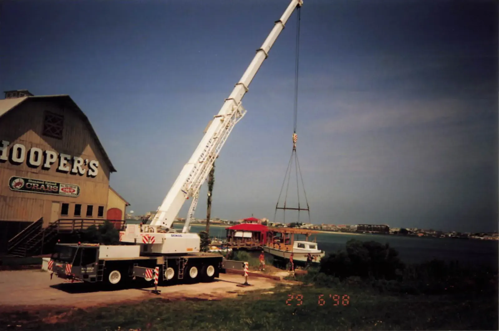 A crane lifting the Sneaky Pete's boat into place beside the Hooper's Crab House building on the water